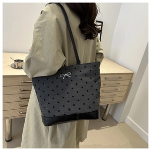 Detailed view of grey polka dot tote bag with bow embroidery worn by a model