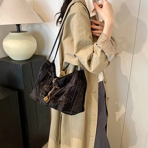 Black pleated tote bag with golden pendant shown on shoulder in modern urban setting