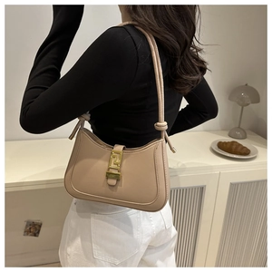 Detail of light beige shoulder bag featuring a gold buckle and decorative knot strap