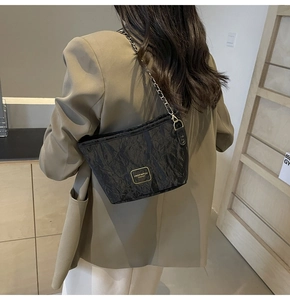 Détail d'un sac bandoulière noir brillant froissé avec chaîne en métal et logo