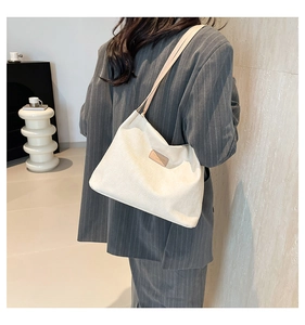 Detailed texture of white vertical ribbed corduroy shoulder bag with leather emblem