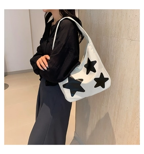 White crescent tote bag featuring three black stars, shown on a model in a warm interior