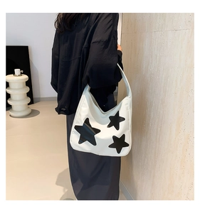 Detail view of large white canvas tote bag with black star prints worn by a model