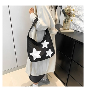 Lifestyle view of a black canvas tote bag with white star prints on a model in trench coat