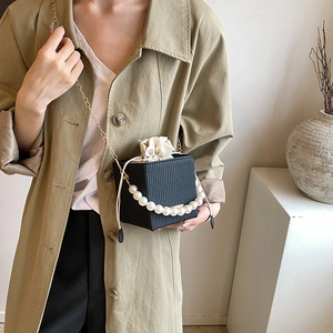 Fashionable black bucket bag with pearl handle and golden chain, elegant pleated texture