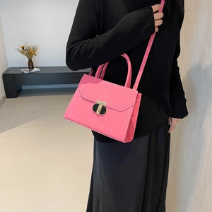 Sac à main rose à texture litchi avec fermoir doré en T porté par un mannequin