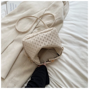 Detail of beige woven crossbody bag showing textured finish and golden hardware