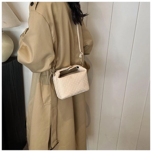 Close-up of cream textured shoulder bag with embossed patterns on trench coat