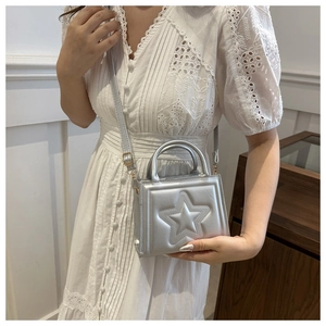 Detail of silver mini square bag with embossed star held by model in white lace dress
