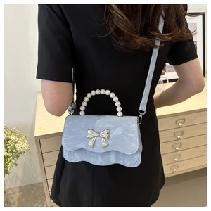 Close-up of light blue textured crossbody bag with pearl handle and silver bow detail