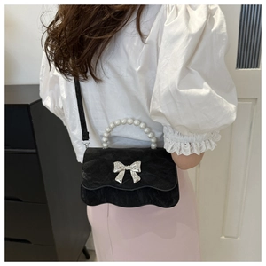 Detail of black velvet shoulder bag with silver bow accent and white pearl top handle