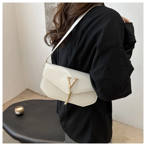 White patent leather shoulder bag detail, featuring shiny metal V clasp and elegant tassel charm.