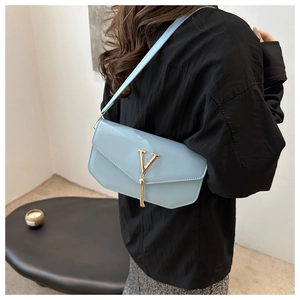 Detail shot of light blue shoulder bag with gold V logo and tassel, elegant daily accessory.
