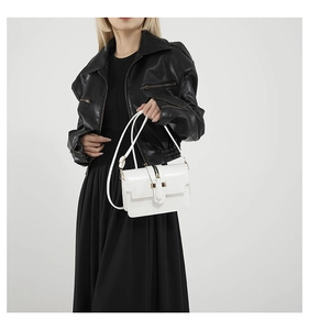 Detail of white patent leather crossbody bag with metal buckle on black dress
