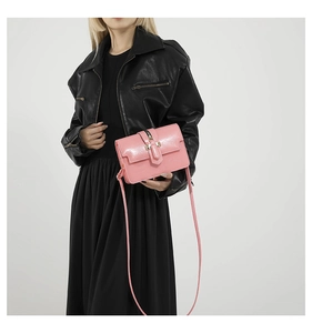 Detail of pink faux leather crossbody bag with gold metallic buckle on a black dress background