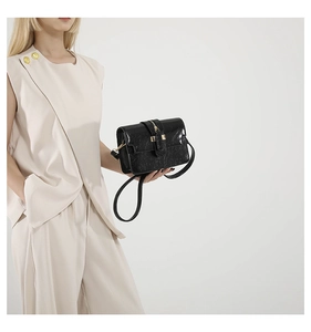 Detail of a chic black textured square bag with gold hardware and stylish leather strap