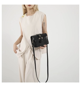 Detail of black crossbody bag with marble texture and gold buckle on a white outfit