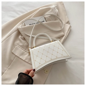 Close-up of white quilted handbag with golden stitching and woven handle detail