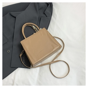 Detail of camel tote bag with cylindrical handle and decorative silk scarf accent