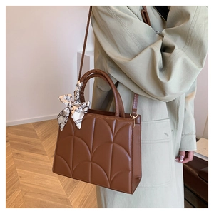 Close-up of brown leather handbag featuring arched stitching and decorative silk scarf detail