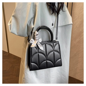 Detail of black quilted tote bag featuring a decorative scarf on the sturdy top handle