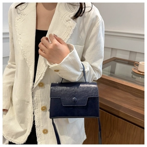 Détail d'un petit sac vintage bleu marine sur un blazer blanc dans un cadre intérieur doux