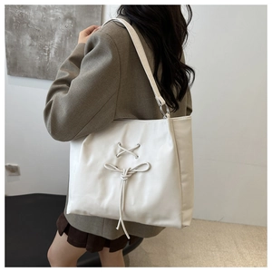 Side view of woman wearing a white tote bag with bow detail and matte leather finish