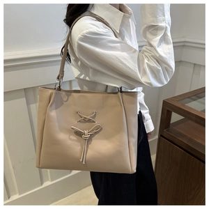 Detail of a large beige tote bag with chic bow tie design on a matte leather surface