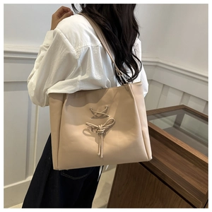 Detail of a beige leather tote bag with a bow accent worn by a model in a modern room