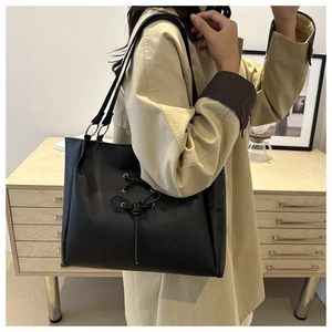 Close-up of black PU leather tote bag featuring bow-tie strap and silver ring hardware