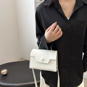 Sac à bandoulière blanc minimaliste en cuir brillant porté par un mannequin dans un cadre épuré