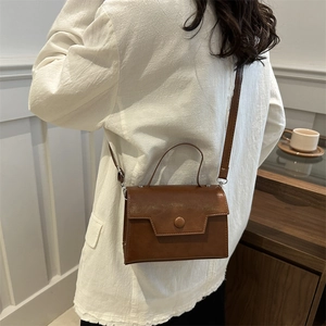 Sac bandoulière vintage marron en simili cuir avec poignée et rabat porté par un modèle
