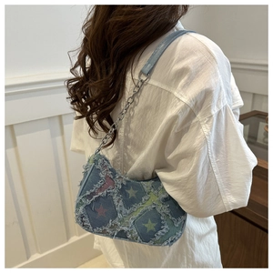 Detail of a crescent denim shoulder bag featuring colorful star patches and frayed edges