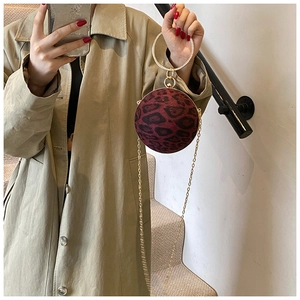 Detail of burgundy leopard print spherical handbag with gold ring handle on beige coat