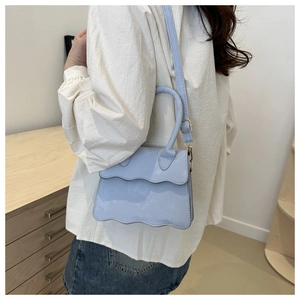 Detail of light blue crossbody bag with scalloped edge flap and gold hardware