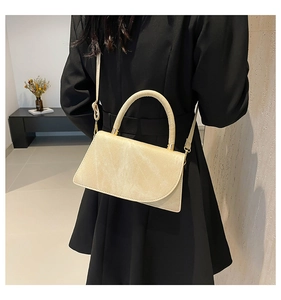 Detail of beige textured mini crossbody bag with curved handle and gold metal hardware