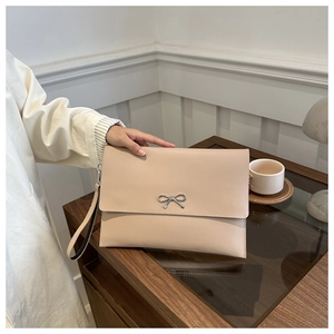 Detail of beige envelope clutch bag with silver metal bow and detachable wrist strap