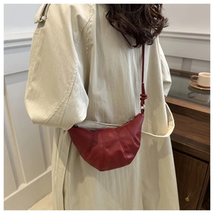 Detailed view of a red croissant bag in matte leather worn with a beige trench coat