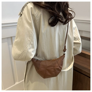 Close-up of a brown leather crescent dumpling bag with vertical decorative stitching on model