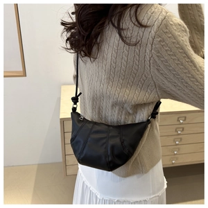 Detail of black pleated croissant bag with knotted shoulder strap worn as a crossbody bag