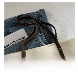 Detail of dark brown leather handle and metal rivets on minimalist canvas tote bag