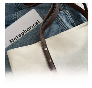 Detail of white canvas tote featuring brown leather handles and silver metal rivets