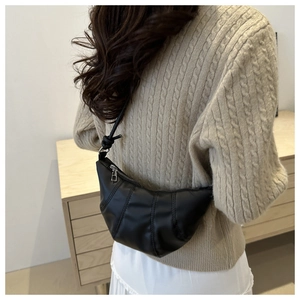 Close-up of black croissant bag with stitched leather detail and knotted shoulder strap