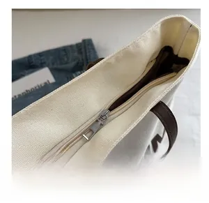 Detail shot of smooth silver metal zipper and brown leather handle on canvas tote bag
