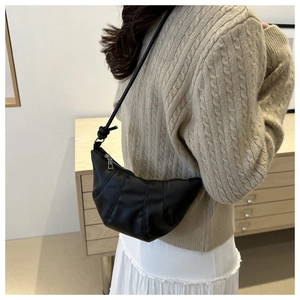 Detail of a black crescent dumpling bag with quilted folds worn with a cozy knit sweater