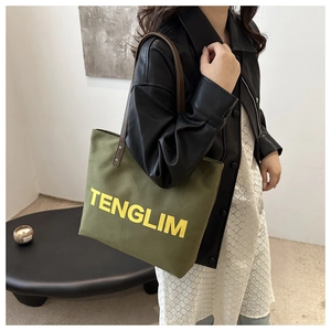 Olive green canvas tote bag with leather straps and yellow text print shown on a model