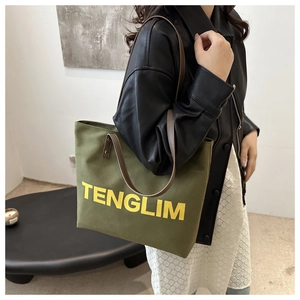 Detail of green canvas tote with brown leather handles and yellow TENGLIM text print