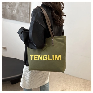Detail of army green canvas tote bag with leather straps and yellow TENGLIM text