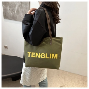 Detail of army green canvas tote bag with brown leather handles and yellow text