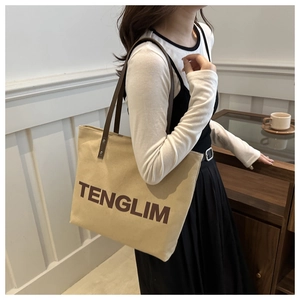 Detail of beige canvas tote bag with brown straps and TENGLIM print shown on shoulder